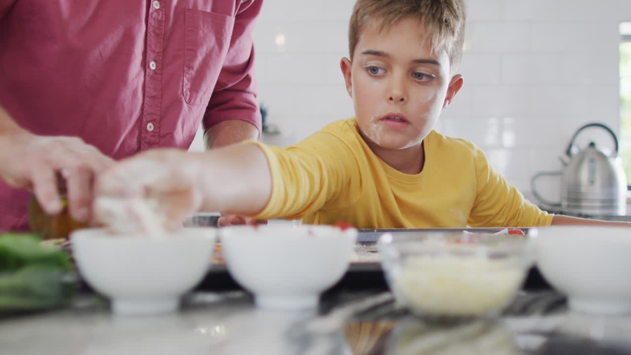 Nonno e nipote caucasici felici che preparano la pizza in cucina, al rallentatore.
