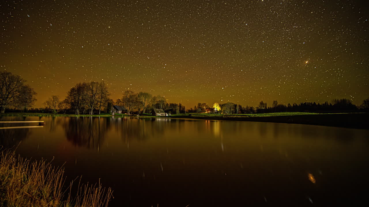 밤에 노란색 검은 색 하늘에서 회전하는 별과 호수 수면에 반사되는 저속 촬영