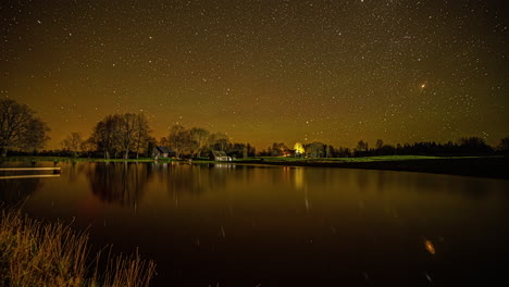 time lapse shot of rotating stars on yellow black colored sky at night and reflection on water surface in lake