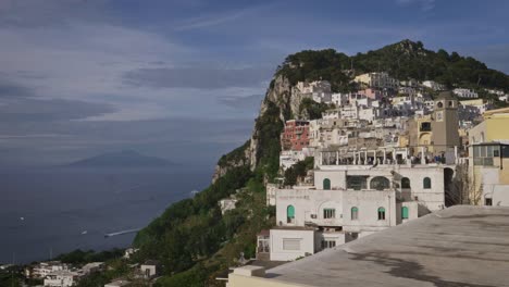 aerial and panoramic view of capri village, piazzetta, sea, vesuvius and boats passing during a sunny day with some clouds