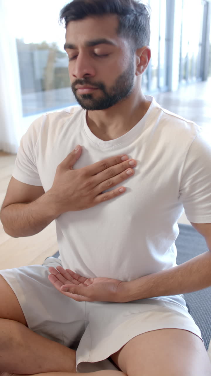 Vertical video of biracial man doing yoga and meditating at home, slow motion