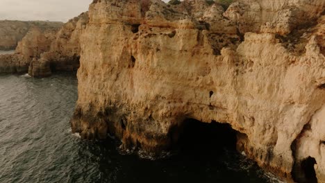 aerial view of dramatic limestone cliffs and sea caves along portugal's algarve coast, bathed in golden light