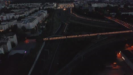 Aerial-view-of-early-morning-train-heading-to-illuminated-train-station.-City-before-sunrise.-Berlin,-Germany