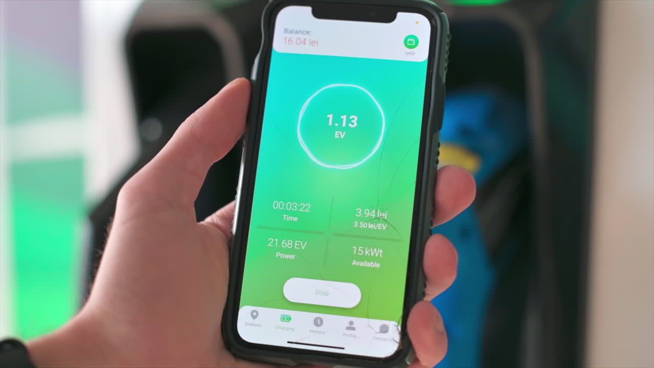 Man charging electro car, holding smartphone with charging process status