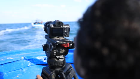 a man shooting a video of the boat in front of him while at sea in the daytime