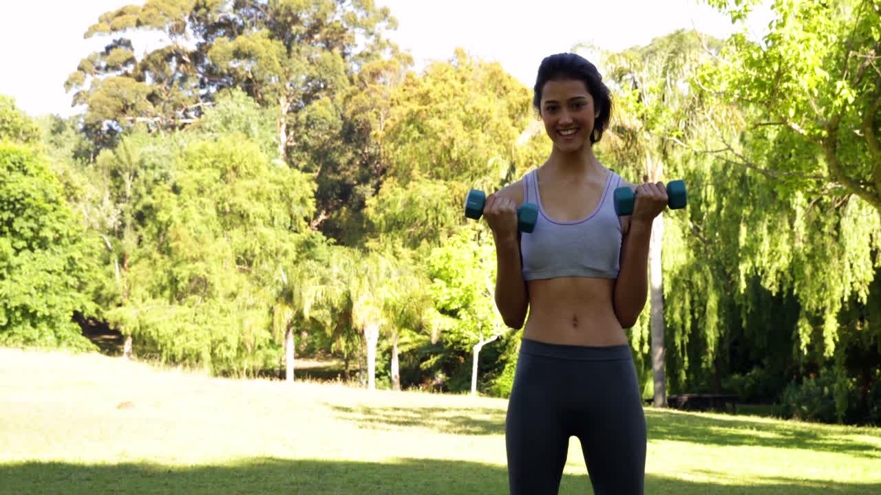 hermosa bruneta en forma levantando pesas con las manos en el parque