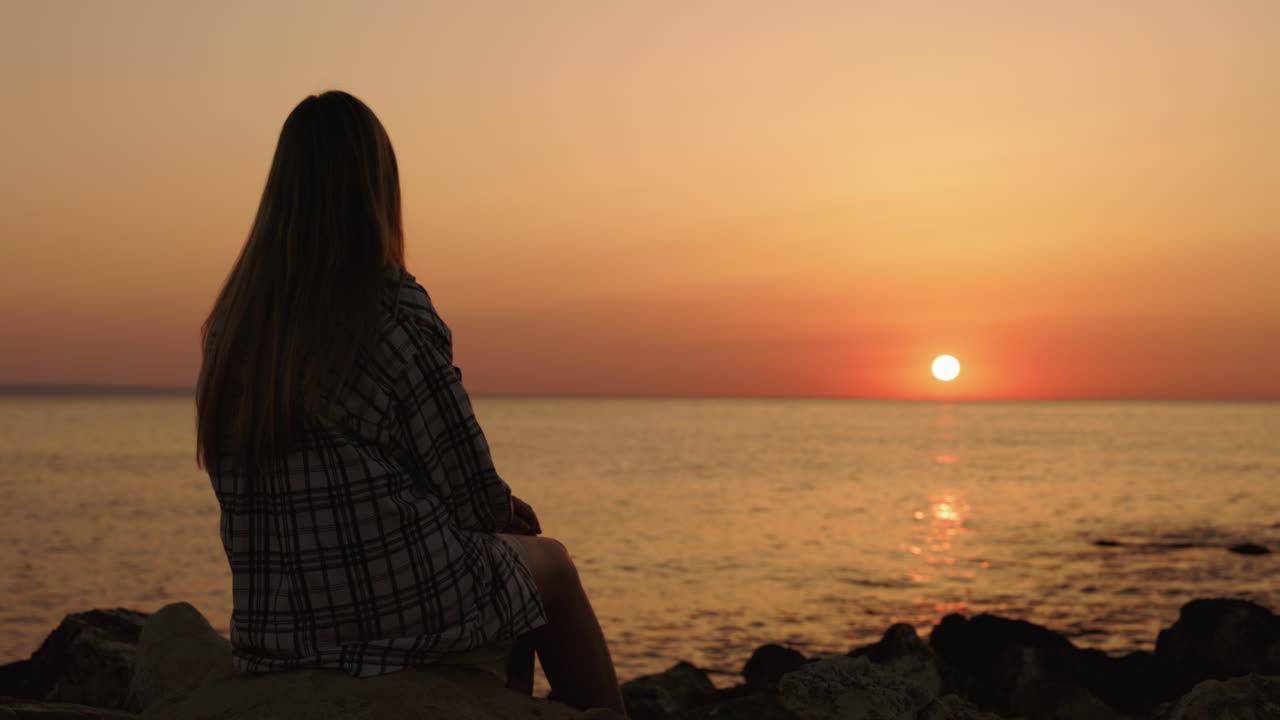 mujer viendo la puesta de sol junto al mar