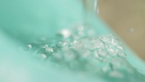 water splashing into a green plastic watering can in slow motion