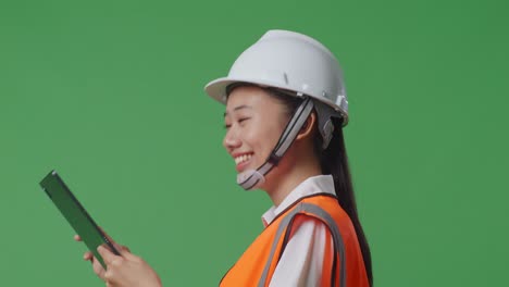 녹색 화면 배경 스튜디오에서 는 동안 태블릿을 사용하는 안전 헬을 입은 아시아 여성 엔지니어