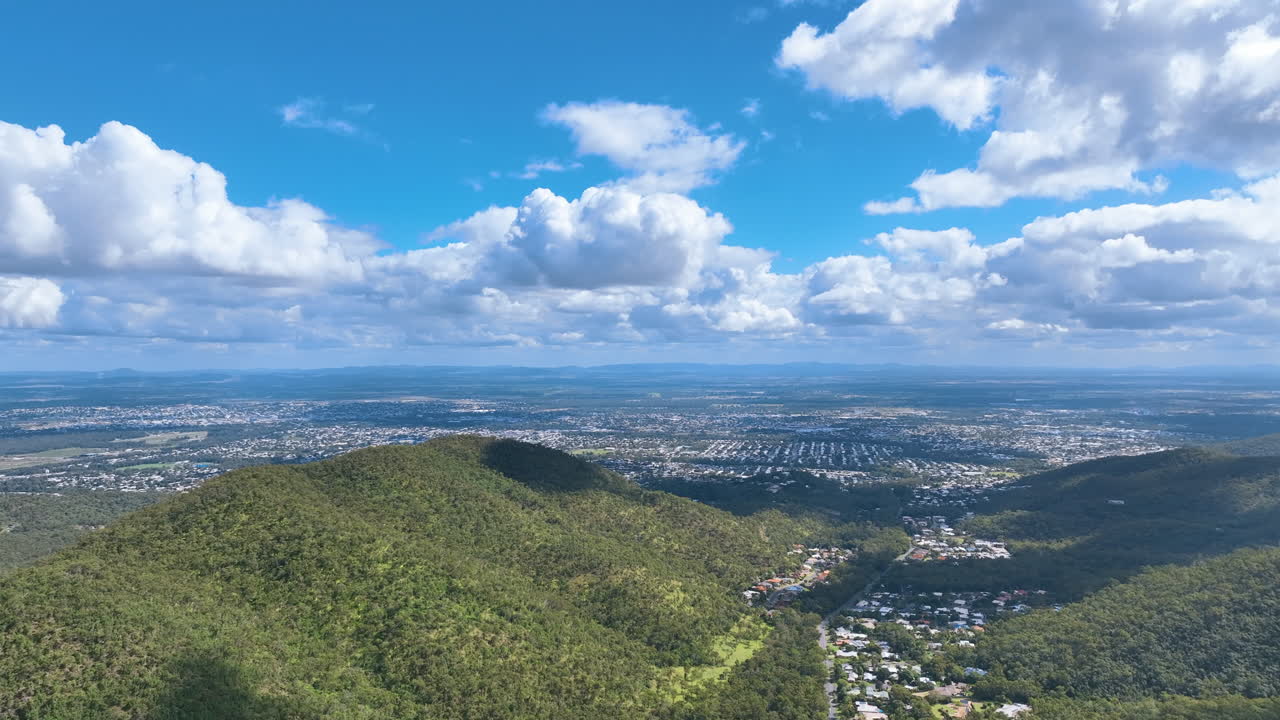 Panoramic aerial from the flanks of Mount Archer above lush foothills, valley suburbs, and out towards the Queensland city of Rockhampton on a stunning day