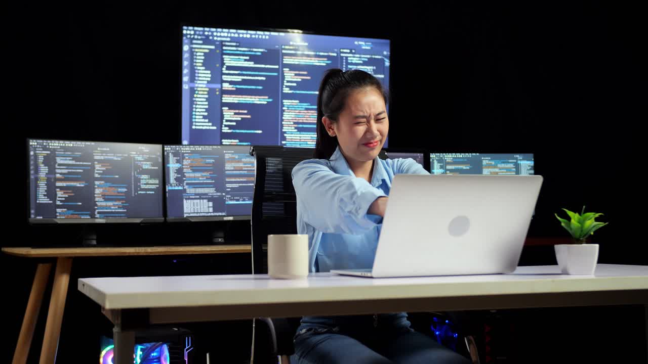 아시아 여성 프로그래머가 여러 모니터를 사용하여 노트북으로 코드를 작성하는 동안 스트레칭하여 사무실의 터미널 창 데스크에서 데이터베이스를 표시합니다.