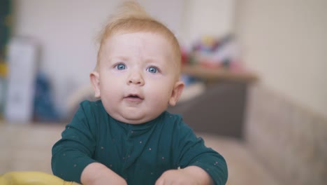 playful baby with blue eyes puts toy in mouth in kid room