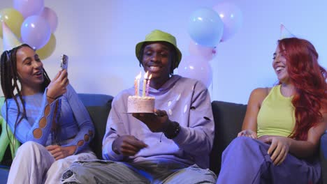 fotografía de estudio de amigos de la generación z celebrando el cumpleaños del hombre con pastel de fiesta y velas sentados en el sofá