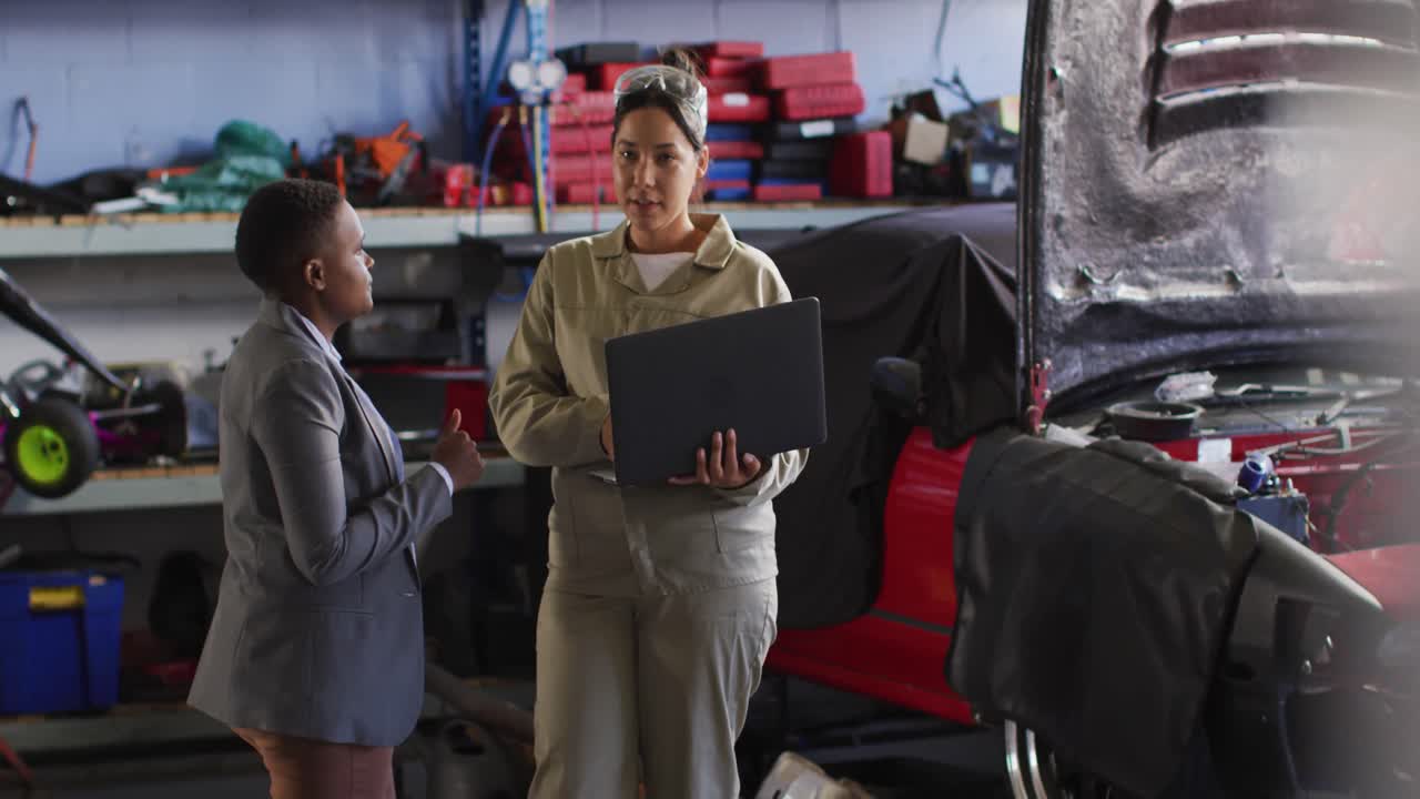 video de dos mecánicos de automóviles diversos y dueño de un negocio con una computadora portátil buscando piezas de automóviles