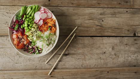 composition of bowl of rice, salmon and vegetables with chopsticks on wooden background