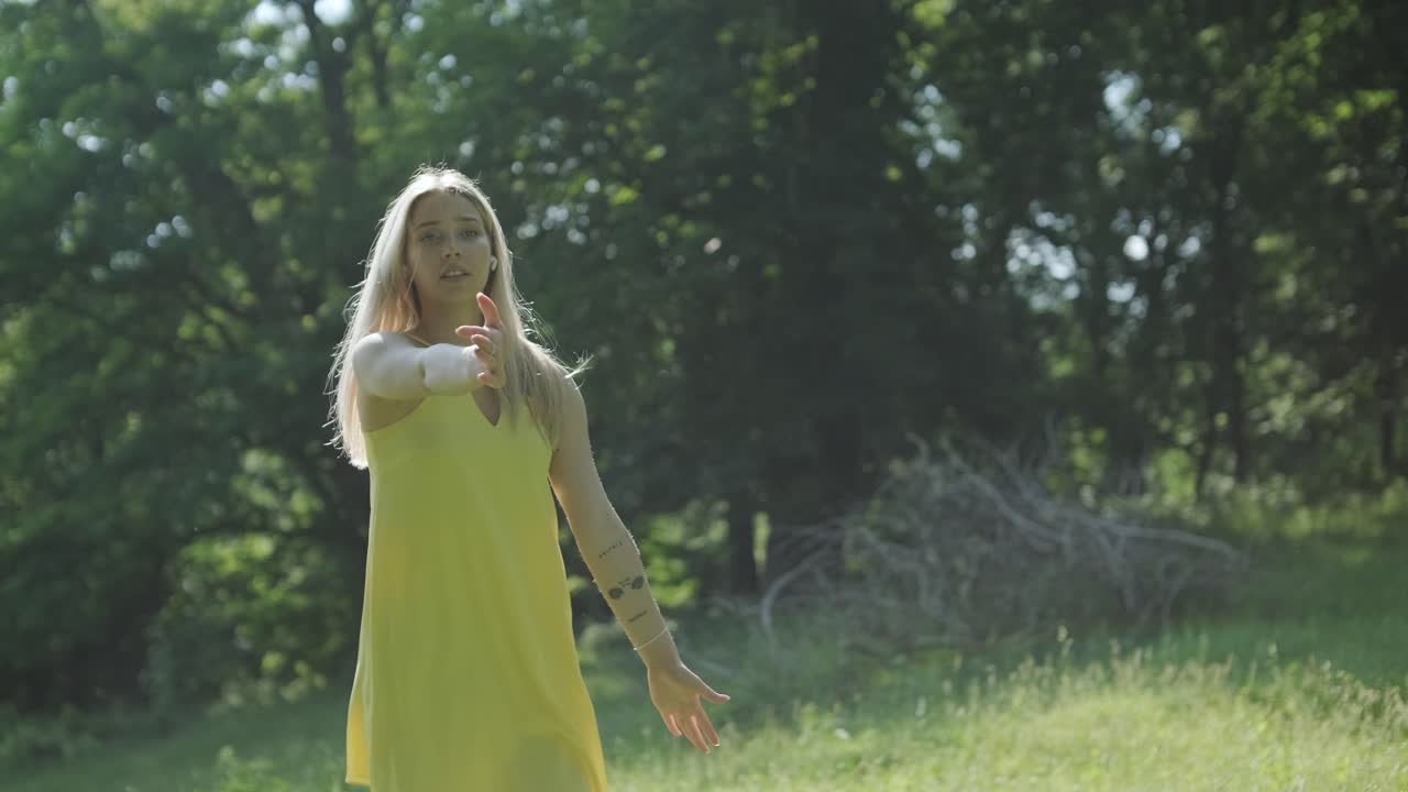 아름다운 젊은 소녀가 자유의 춤을 추고 있습니다. 여름 공원에서 뒷면에 나무가 있습니다.