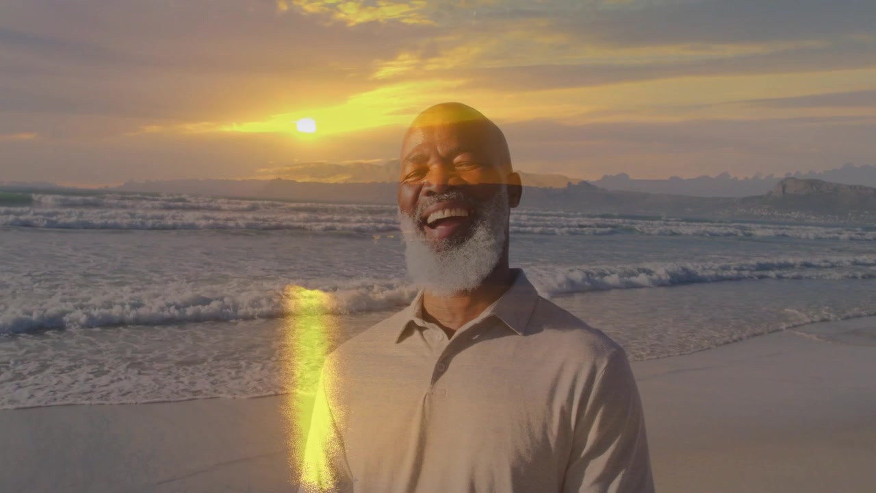 Senior man standing on beach, sun flare crossing face causing laughter for travel marketing