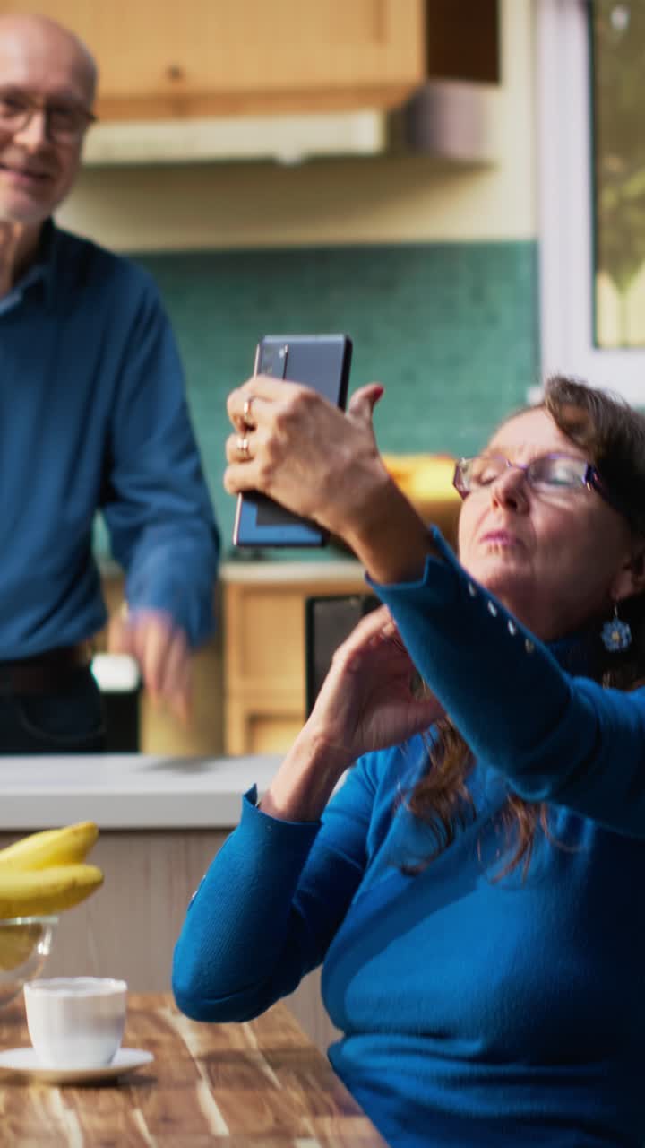 Vertical Video Elderly woman acting silly and taking pictures of herself in the kitchen