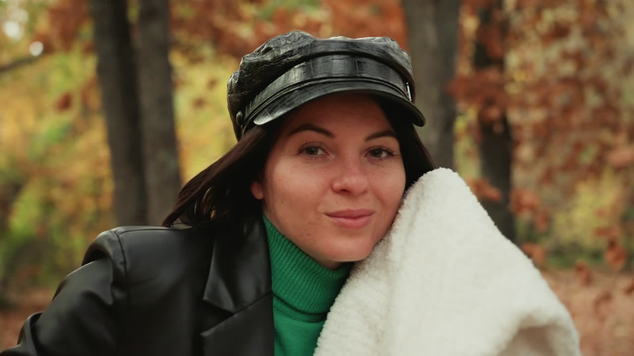 woman with cozy blanket in woods, intimate closeup shows soft fleece draped over shoulder, green sweater and leather jacket, warm smile and gentle breeze, hygge lifestyle vibe for seasonal content