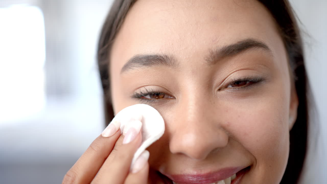 Smiling woman cleaning face with cotton pad, focusing on skincare routine