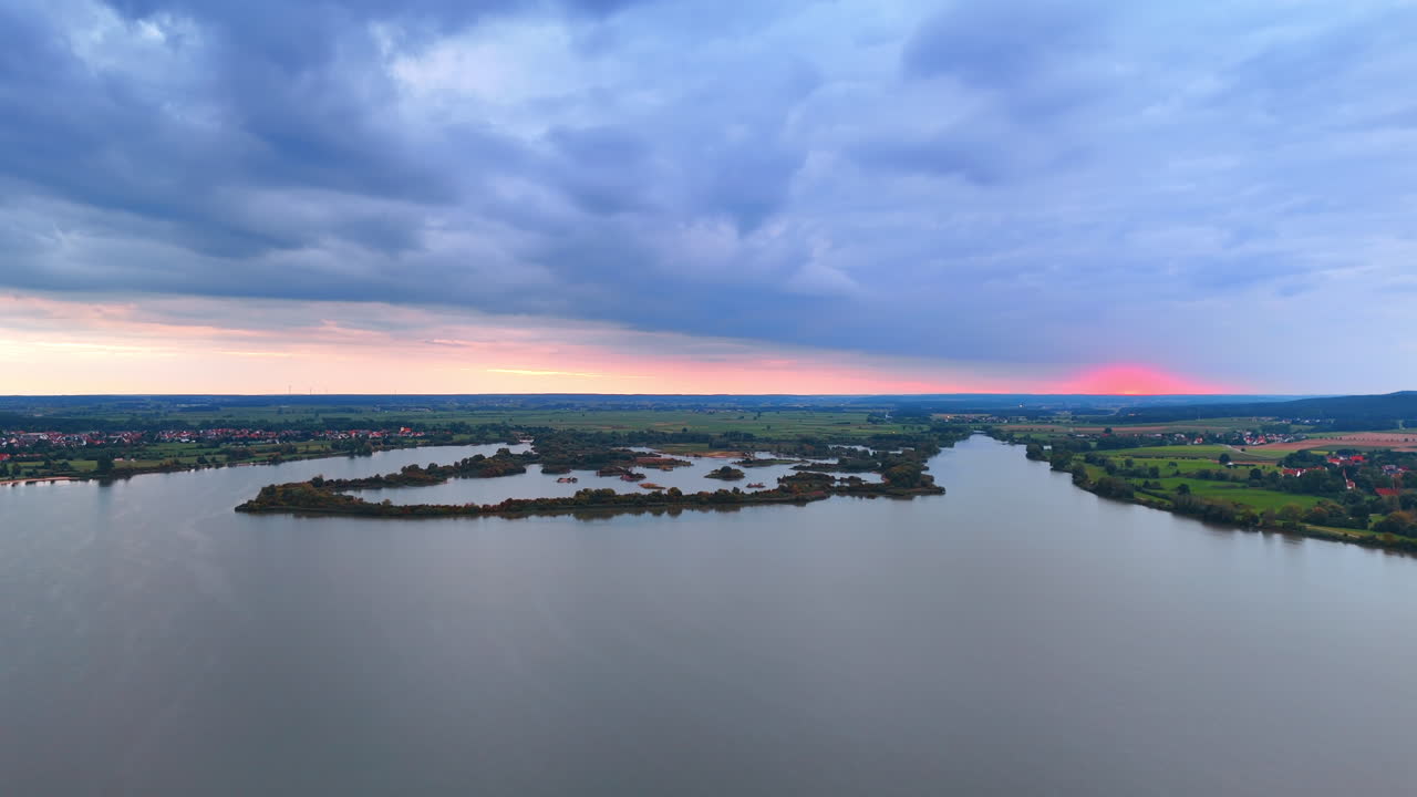Tramonto sul lago Altmühlsee con isole santuario degli uccelli. Vista panoramica della superficie del lago, isole naturali e un tramonto rosa vivace all'orizzonte sotto nuvole pesanti.