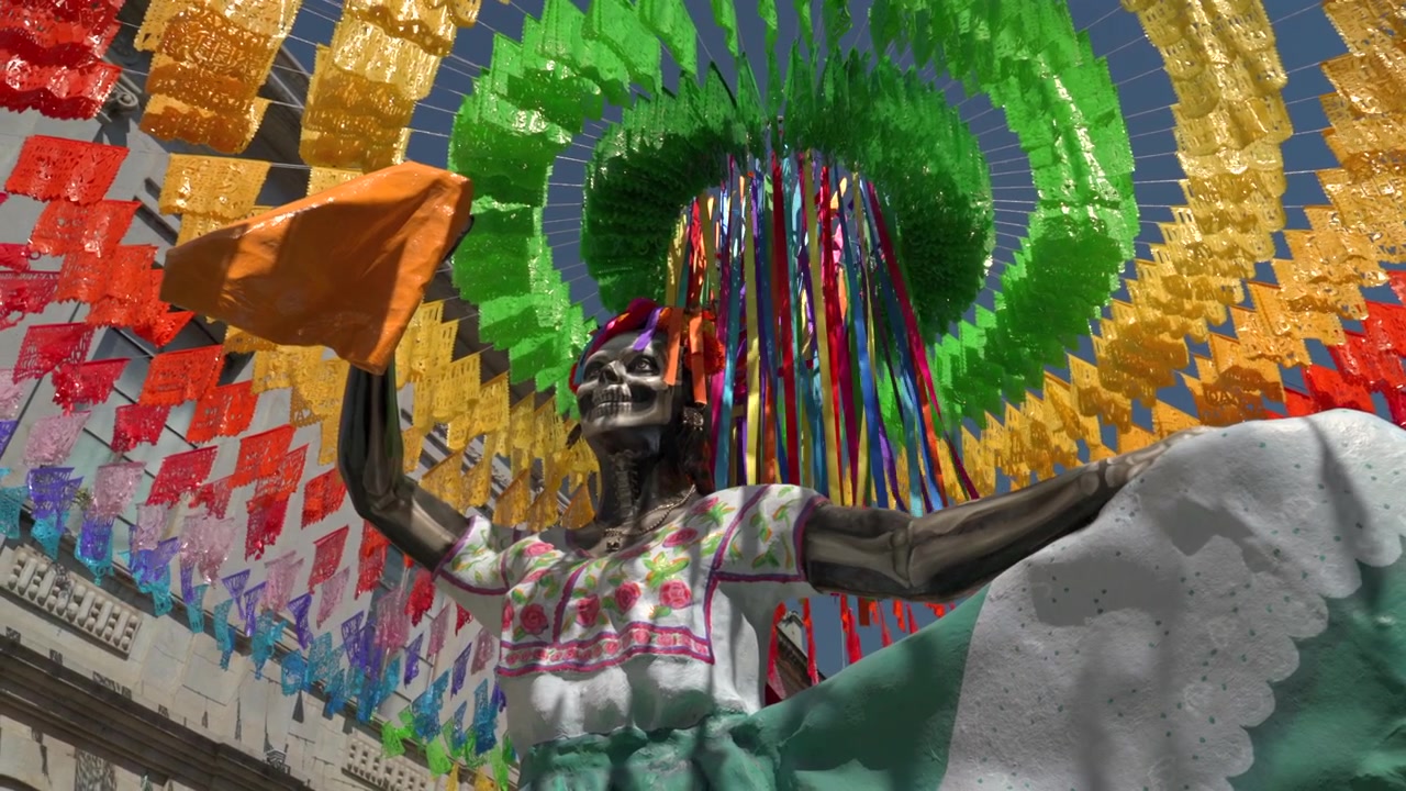 Inquadratura dal basso di una tradizionale figura scheletrica della Catrina sotto vivaci papel picado messicani e nastri all'aperto, alla luce del giorno.