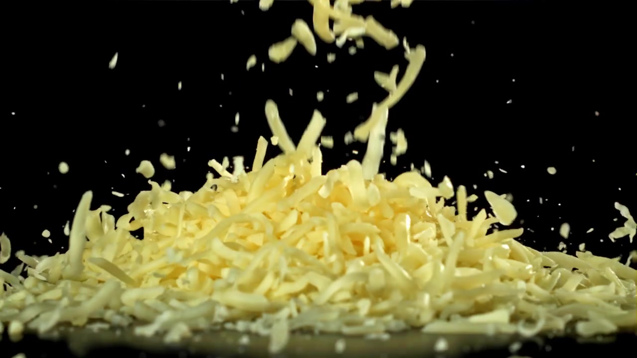 Formaggio grattugiato che cade al rallentatore su sfondo nero.