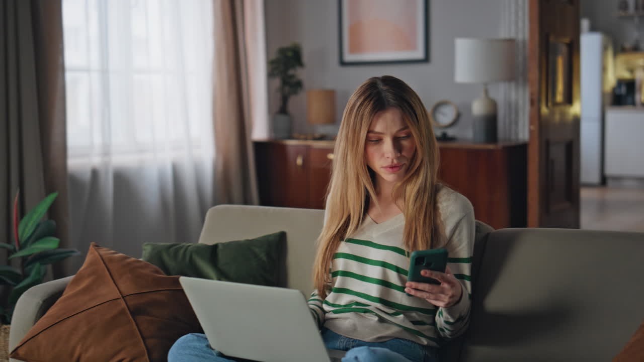 Relaxed lady surfing laptop on couch living room. Calm woman looking smartphone