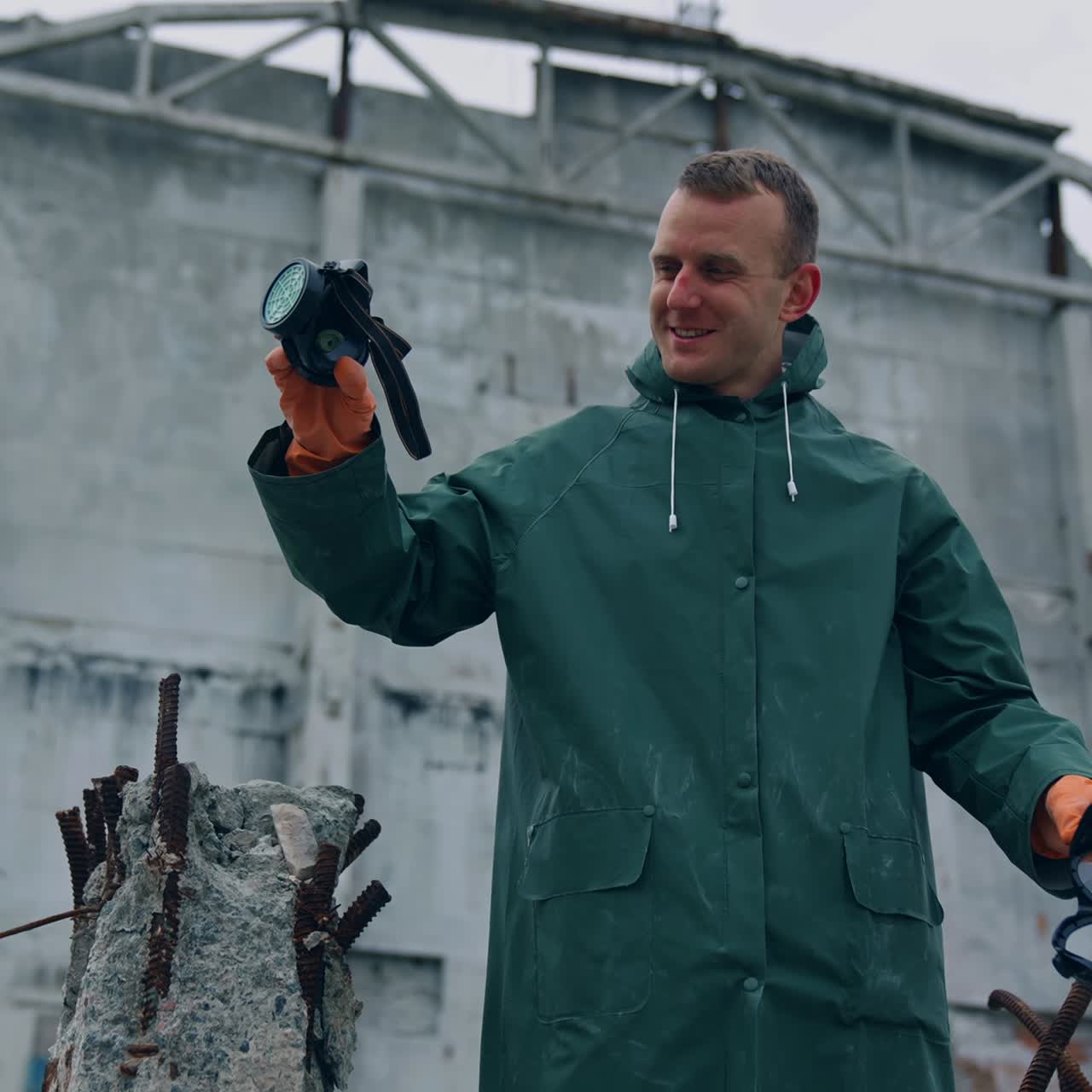 Happy ecologist in abandoned place. Man survivor holding gas mask in hands and smiles breathing fresh air on the background of destroyed building