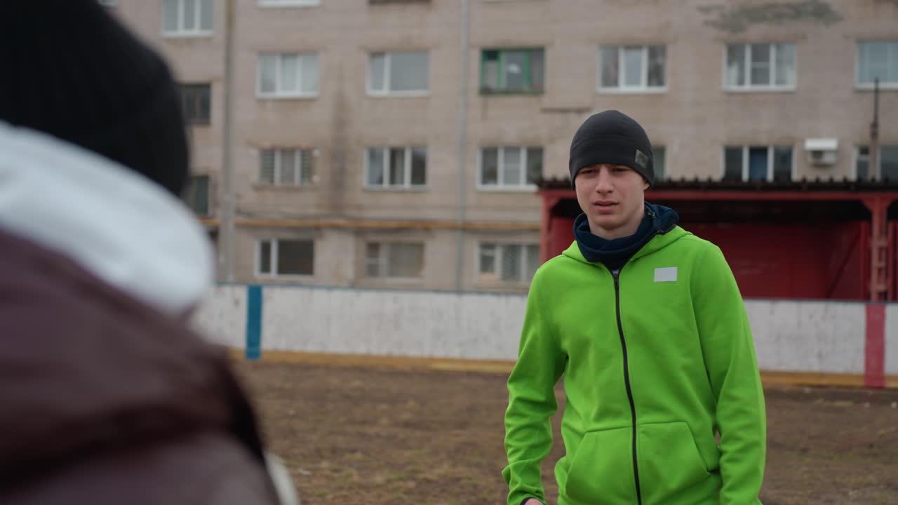 Hombre caucásico recibe el balón de su entrenador en un campo de barrio, intercambio de instrucciones y pases al anochecer con frío, trabajo en equipo y entrenamiento de base, expresión atenta y lección práctica