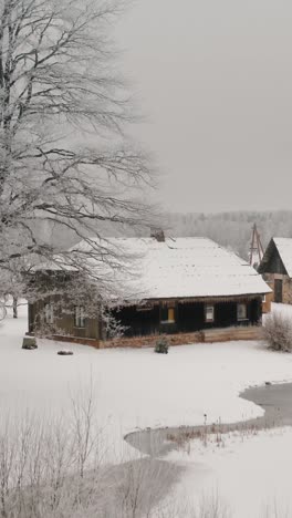 Vertical drone shot of a family house in the countryside during winter with lots of snow and frost on the trees. Winter wonderland in historic suburb area.