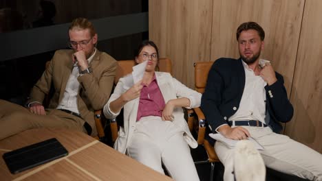 Tired-of-the-heat,-employees-of-a-modern-office-in-business-suits-sit-at-the-table,-leaning-on-the-back-of-the-chair-and-resting.-A-hard-day-at-work-in-a-hot-modern-office.-Two-guys-and-a-girl-in-business-suits