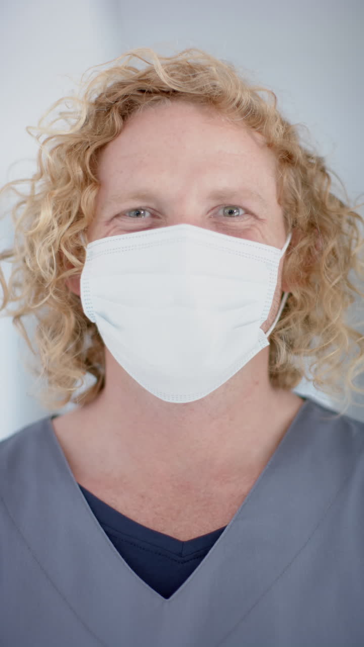 Vertical video of portrait of happy caucasian male doctor wearing face mask, slow motion