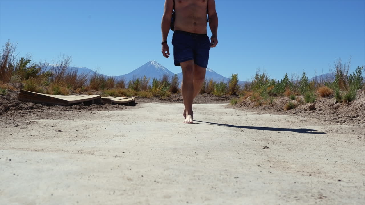 hombre caucásico descalzo en pantalones cortos de baño camina por un camino de tierra remoto en chile