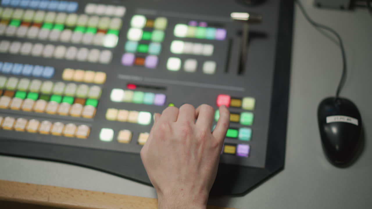 Close-up of hand operating control panel with colored buttons in TV production control room. Focused operator using video switcher in live broadcast or media production studio environment