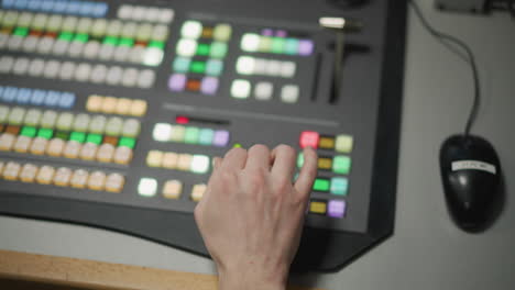 close-up of hand operating control panel with colored buttons in tv production control room. focused operator using video switcher in live broadcast or media production studio environment