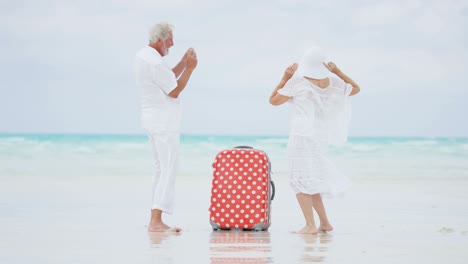 caucasian seniors on beach with camera and suitcase