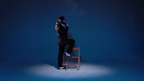 stylish man posing with chair and smoking in a blue studio setting
