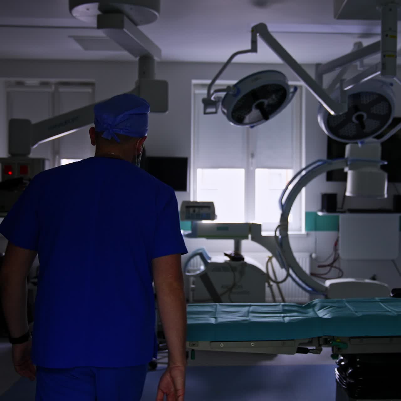 Male anesthesiologist comes up to a door with a window leading to a modern surgical theatre. Doctor enters the room and the light switches on