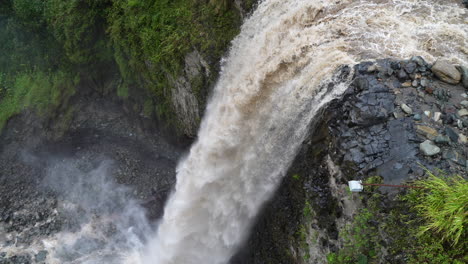 antena arriba hacia abajo mostrando una gigantesca cascada estrellándose por el acantilado en la selva de ecuador - vista de pájaro en cámara lenta