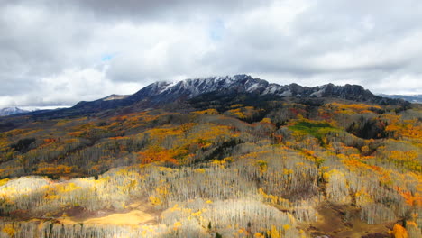 dramatic cloudy autumn aspen tree fall colors kebler pass trailhead aerial cinematic drone snow on peaks landscape crested butte gunnison colorado early fall red yellow orange rocky mountains upward