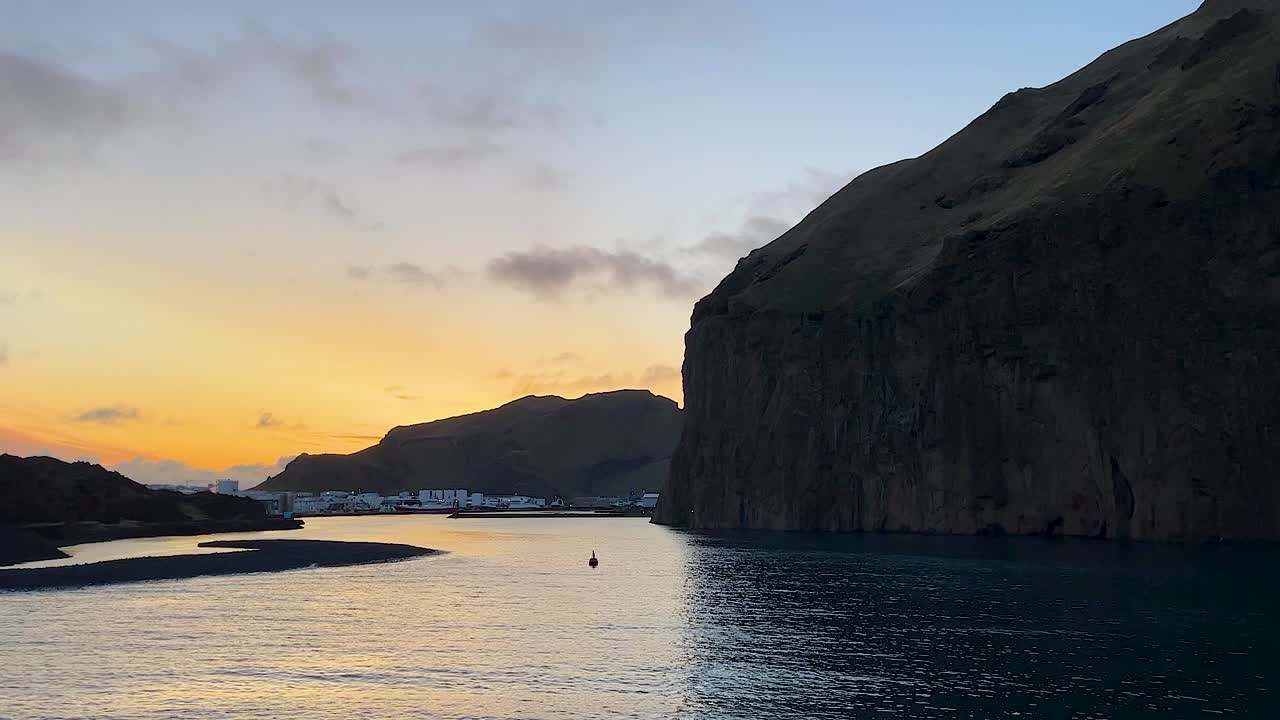 puesta de sol sobre el puerto de vestmannaeyjar con aguas tranquilas y acantilados dramáticos