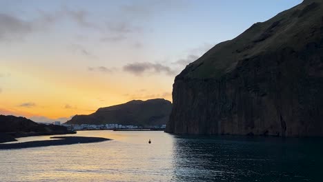 sunset over vestmannaeyjar port with calm waters and dramatic cliffs