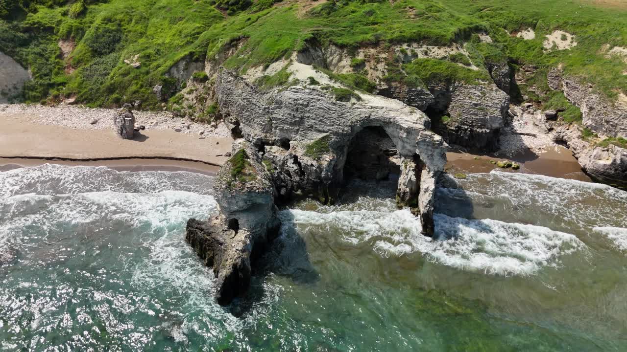 Drone view of rocky coast with waves crashing on a sunny day