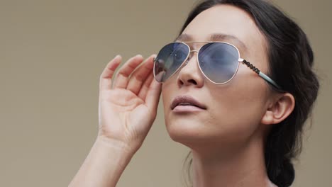 mujer asiática con cabello oscuro y gafas de sol con espacio de copia en fondo beige, cámara lenta