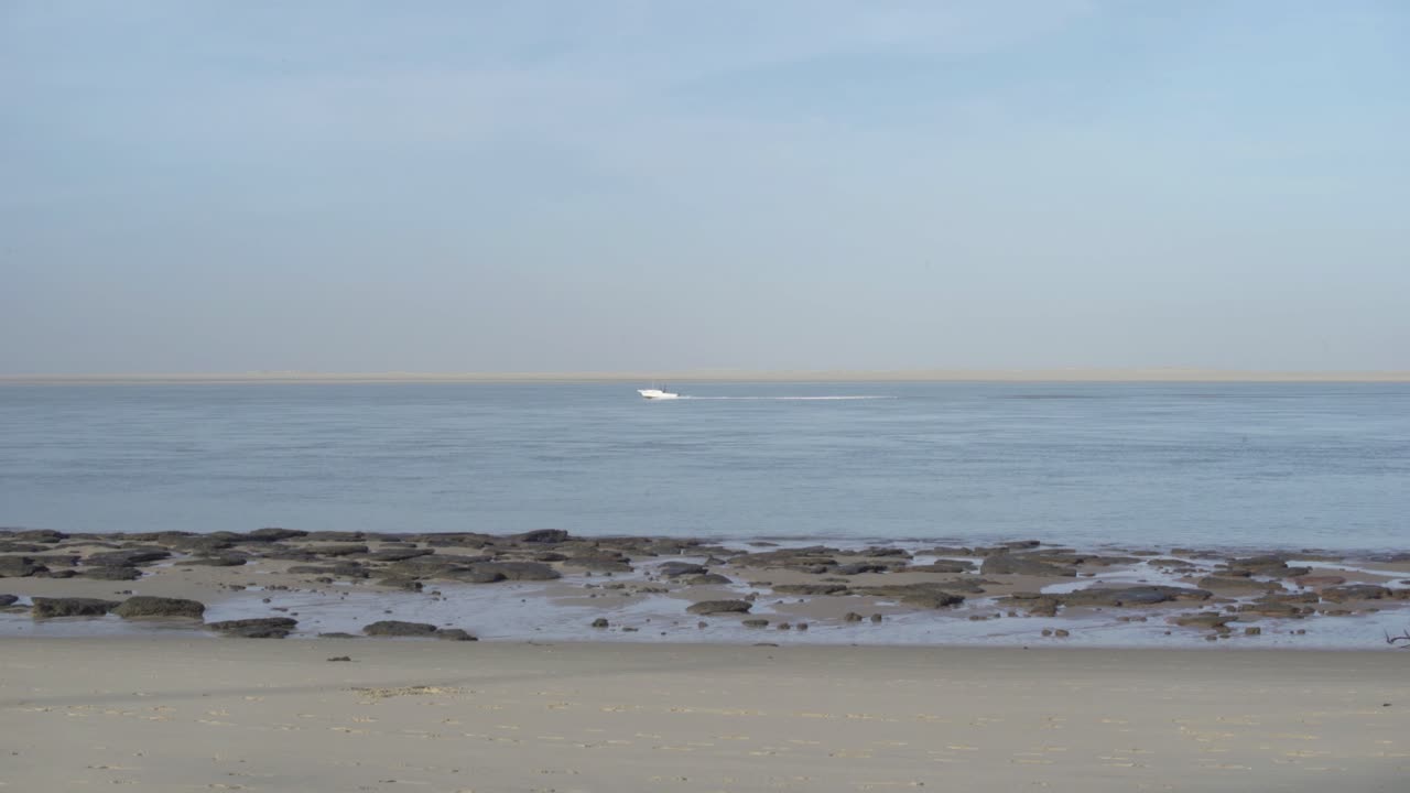 Sea view from the beach. Boat passing over the horizon. Early morning. Low tide. Sunny