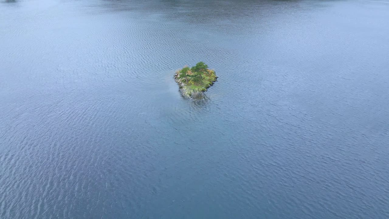 fotografía de un avión no tripulado que se acerca de una pequeña isla en el medio del lago olswater, un lago glacial en cumbria, inglaterra y parte del parque nacional del distrito de los lagos en el reino unido