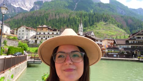 close up of woman face with hat enjoying lago di alleghe, village in background