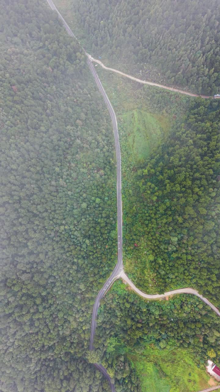 Vertical aerial view of the lush hills and winding roads in the Guizhou Province, China. Showcasing scenic mountain terrain surrounded by dense forest, perfect for nature and travel content