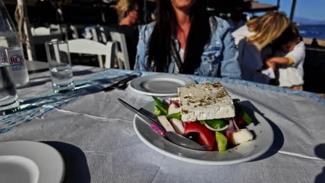 Close-up-of-a-fresh-Greek-salad-with-feta-cheese-on-a-sunny-day-with-women-enjoying-her-holiday,-perfect-for-a-healthy-meal-concept